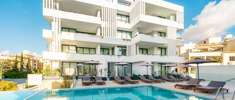 A modern hotel with a pool area, multiple balconies, and lounge chairs.