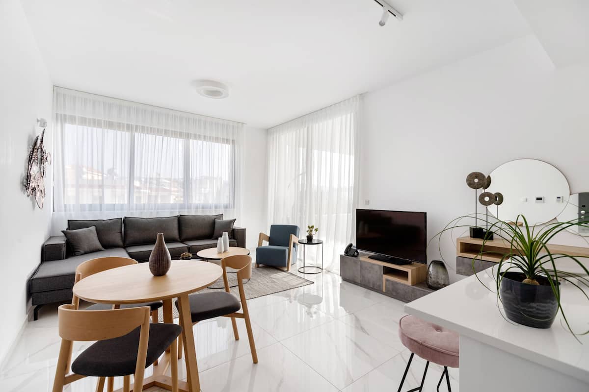 Una sala de estar moderna con un sofá, una mesa de comedor, sillas, un televisor y una planta en maceta.