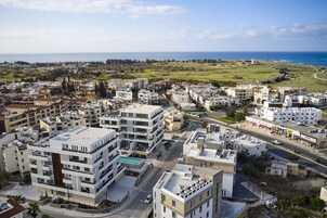 Un paisaje costero urbano con edificios modernos, una vista despejada del mar y un faro a lo lejos.