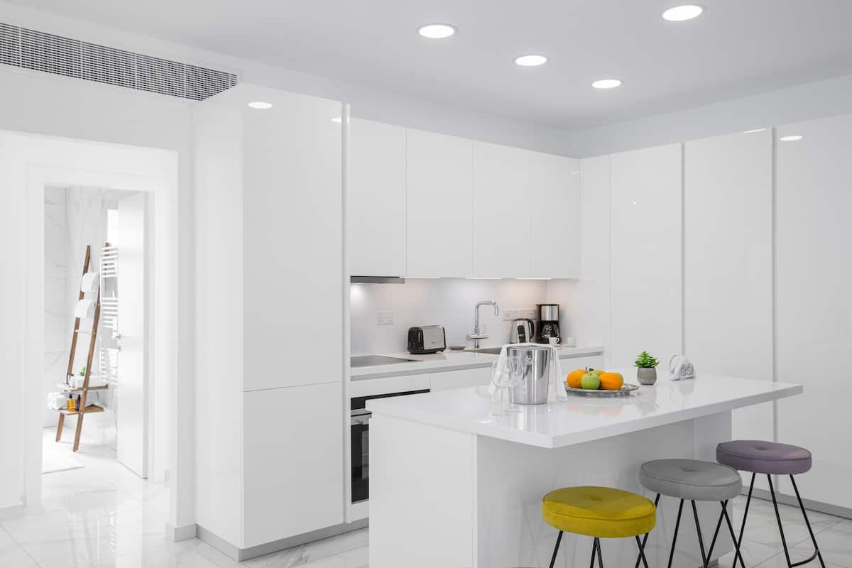 Una cocina moderna con armarios blancos, una isla central con taburetes y un tostador.