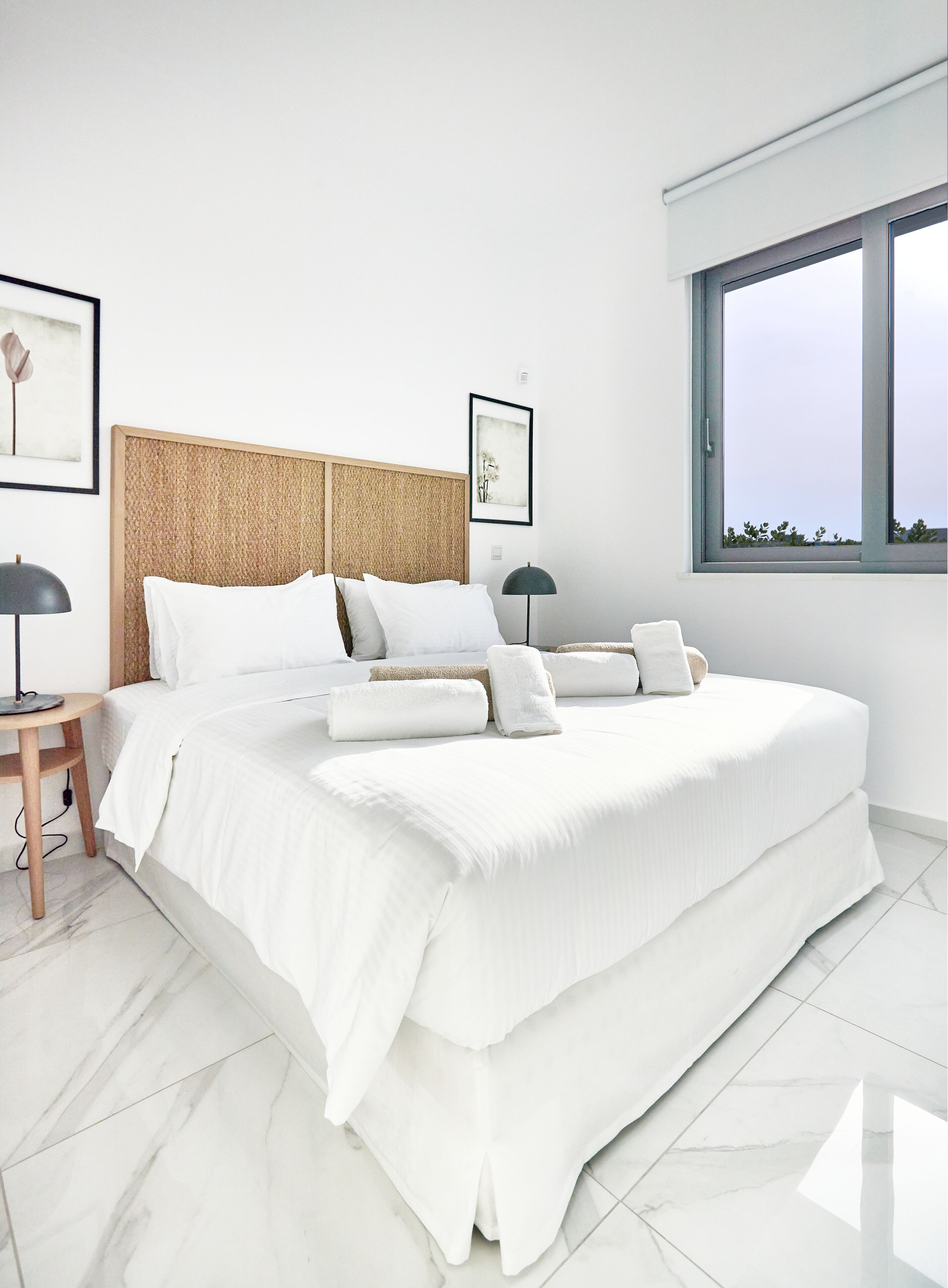 Un dormitorio moderno con una cama grande, un cabecero de textura tejida, una mesita de noche con una lámpara y una ventana con vistas.