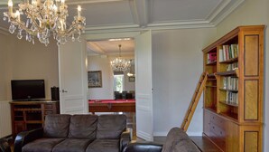 A living room with a dark leather sofa, a wooden coffee table, a bookshelf, and a chandelier. - Lavish Castle in Thimister with Turkish Steambath, Sauna (Thimister-Clermont)
