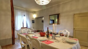 A dining room with a table set for four, white chairs, a chandelier, and a window with curtains.