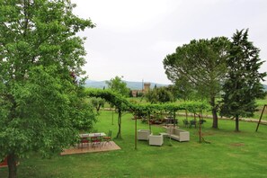 Un espace extérieur verdoyant, avec une table et des chaises, une pergola et une vue sur des collines lointaines.