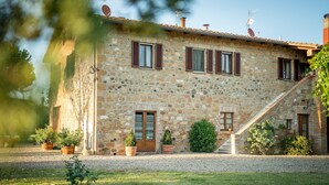 A stone house with a gravel driveway, wooden shutters, and potted plants.