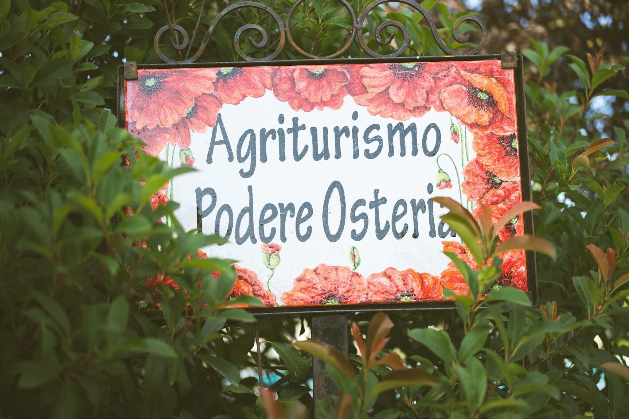 A sign with the text "Agriturismo Podere Osteria" surrounded by red flowers.