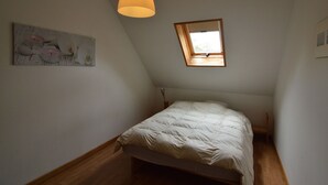 A bedroom with a sloped ceiling, a single bed, a hanging light fixture, a skylight, and a painting on the wall.