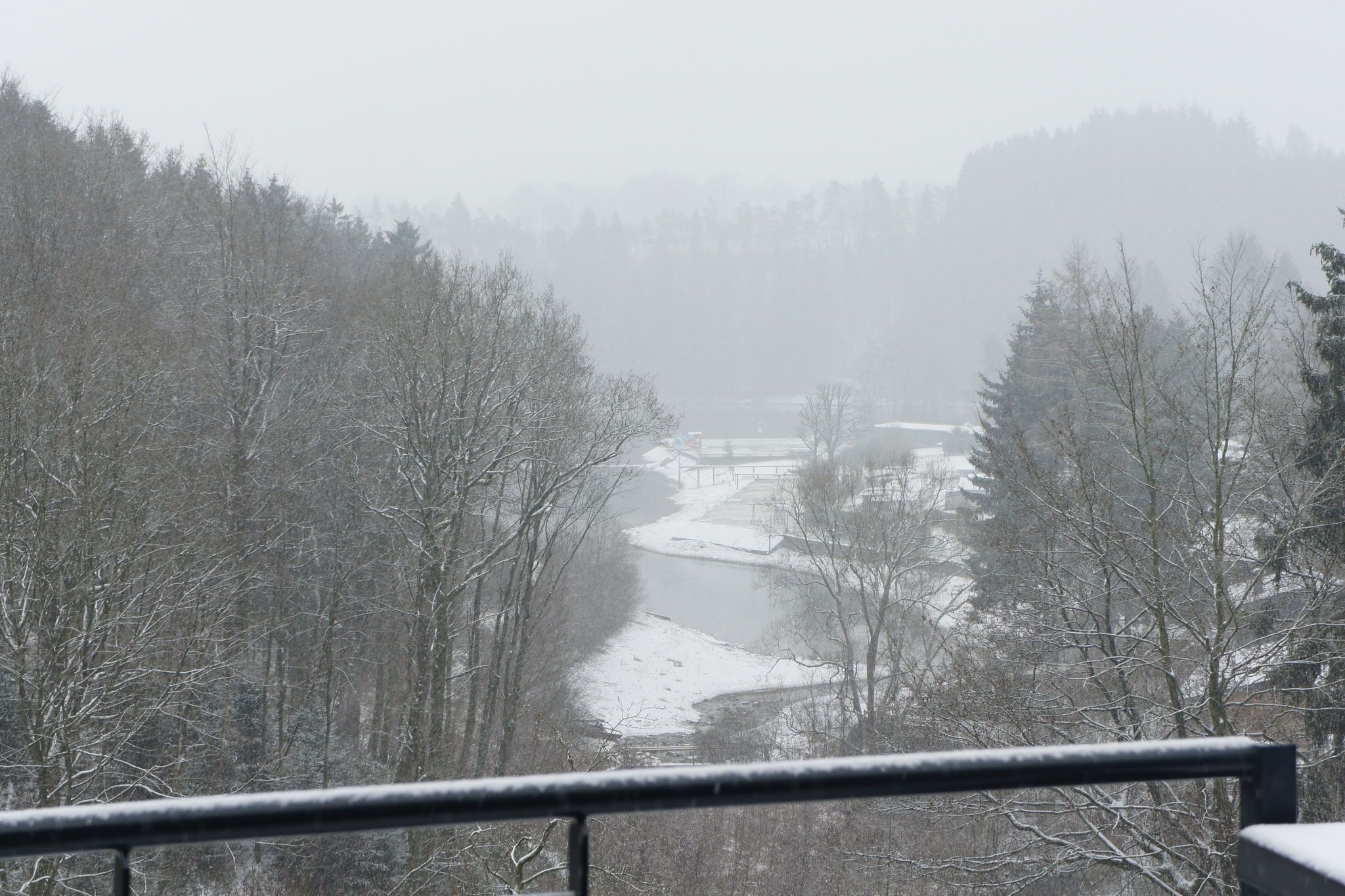 Paisagem coberta de neve com um rio, árvores e uma ponte.