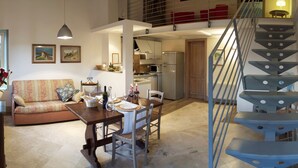 A spacious living area with a dining table set for two, a sofa, and a staircase leading to an upper level. - Farmhouse in San Gimignano with Pool (San Gimignano)