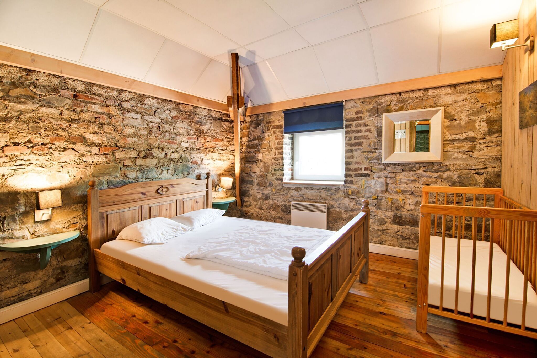A bedroom with a wooden bed, stone walls, a wooden crib, and a window with a view.