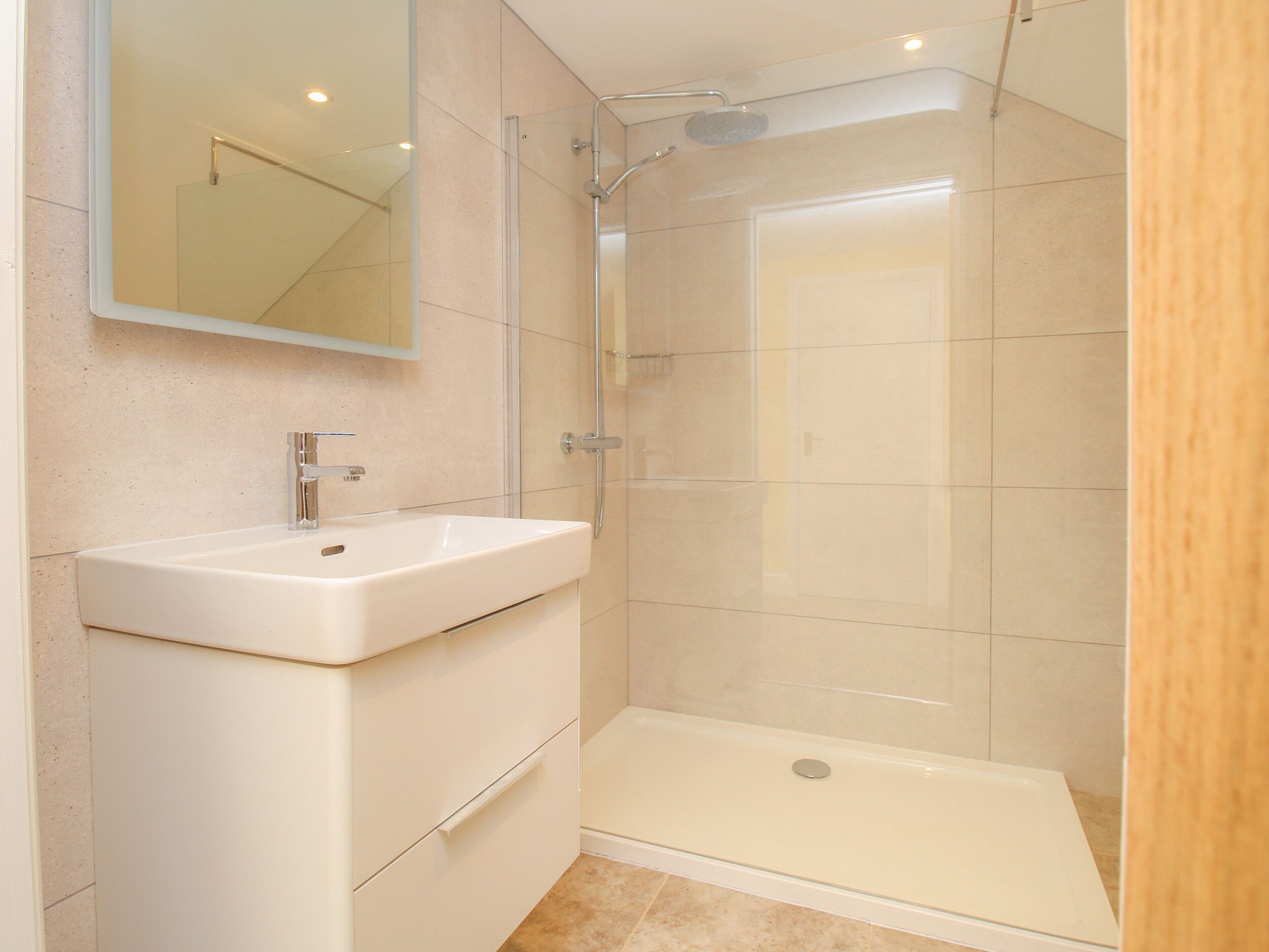 Ein modernes Badezimmer mit einer gläsernen Dusche, einem weißen Waschbecken und einem Spiegel.