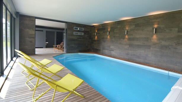 Piscina interior moderna con cubierta de madera y sillas reclinables amarillas.