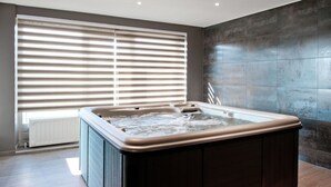 A modern bathroom with a freestanding hot tub, large windows with blinds, and a dark tiled wall. - Swanky Holiday Home in Waimes with Indoor Swimming Pool (Waimes)