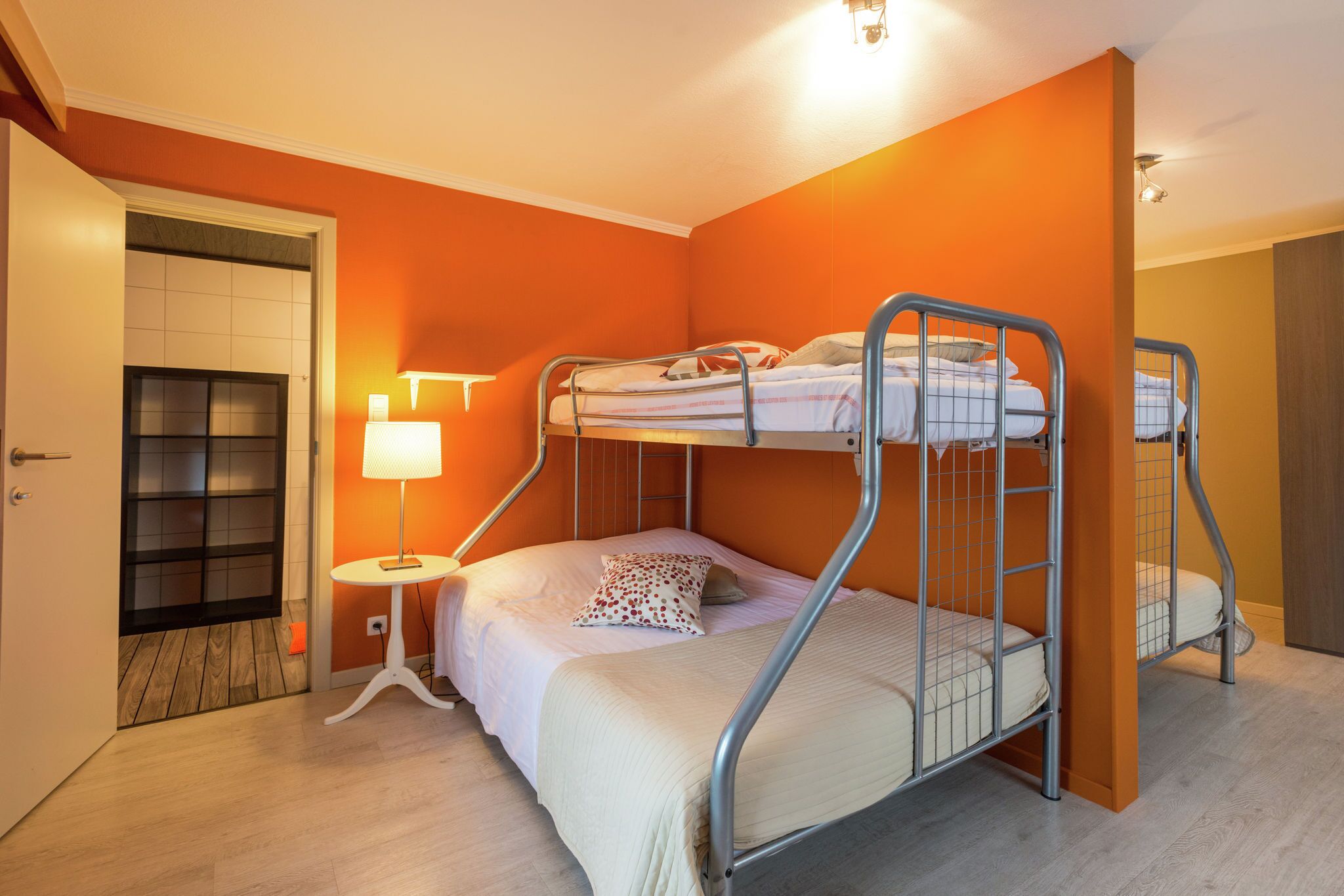Ein Zimmer mit einem Etagenbett, einem kleinen Tisch mit einer Lampe und einer Tür zu einem weiteren Raum.