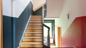 A staircase with wooden steps and a metal railing, leading to a room with a green door and a window.