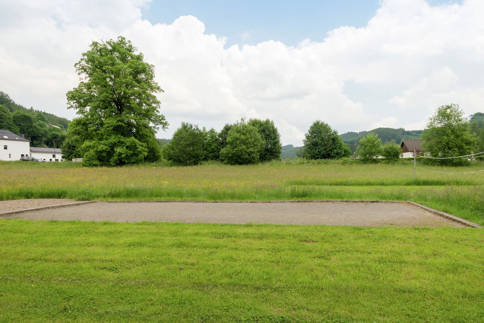 Eine Wiese mit befestigtem Bereich, umgeben von Bäumen und Häusern in ländlicher Umgebung.