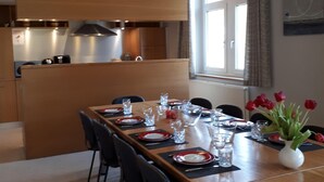 A dining area with a long table set for four, equipped with plates, glasses, and cutlery. There is a vase with red tulips on the table.