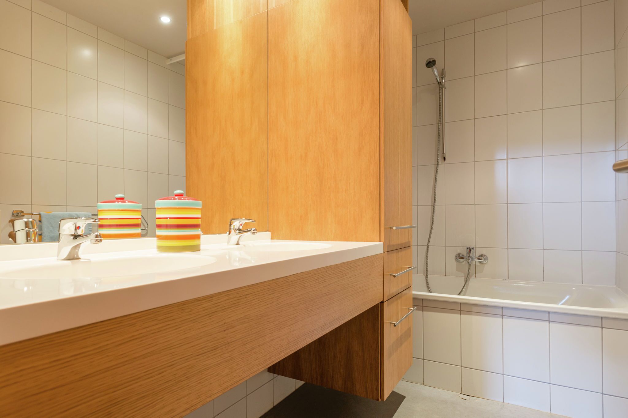 Ein modernes Badezimmer mit einem Holzbadezimmerunterschrank, einem weißen Waschbecken, zwei gestreiften Seifenspendern, einer Dusche und einer Badewanne.