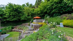A garden with a wooden fence, a stone pathway, and an orange umbrella. - Holiday Home in Malmedy with Sauna & Bubble Bath (Malmedy)