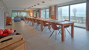 Een moderne eethoek met een lange tafel, stoelen en uitzicht op zee.