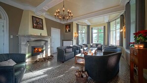A spacious living room with a fireplace, multiple seating areas, and large windows allowing natural light.