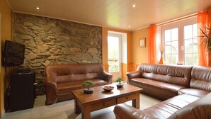 Ein Wohnzimmer mit einer Steinwand, zwei braunen Ledersofas, einem Couchtisch mit Bonsai-Bäumchen und einem Fernseher auf einem Schrank.