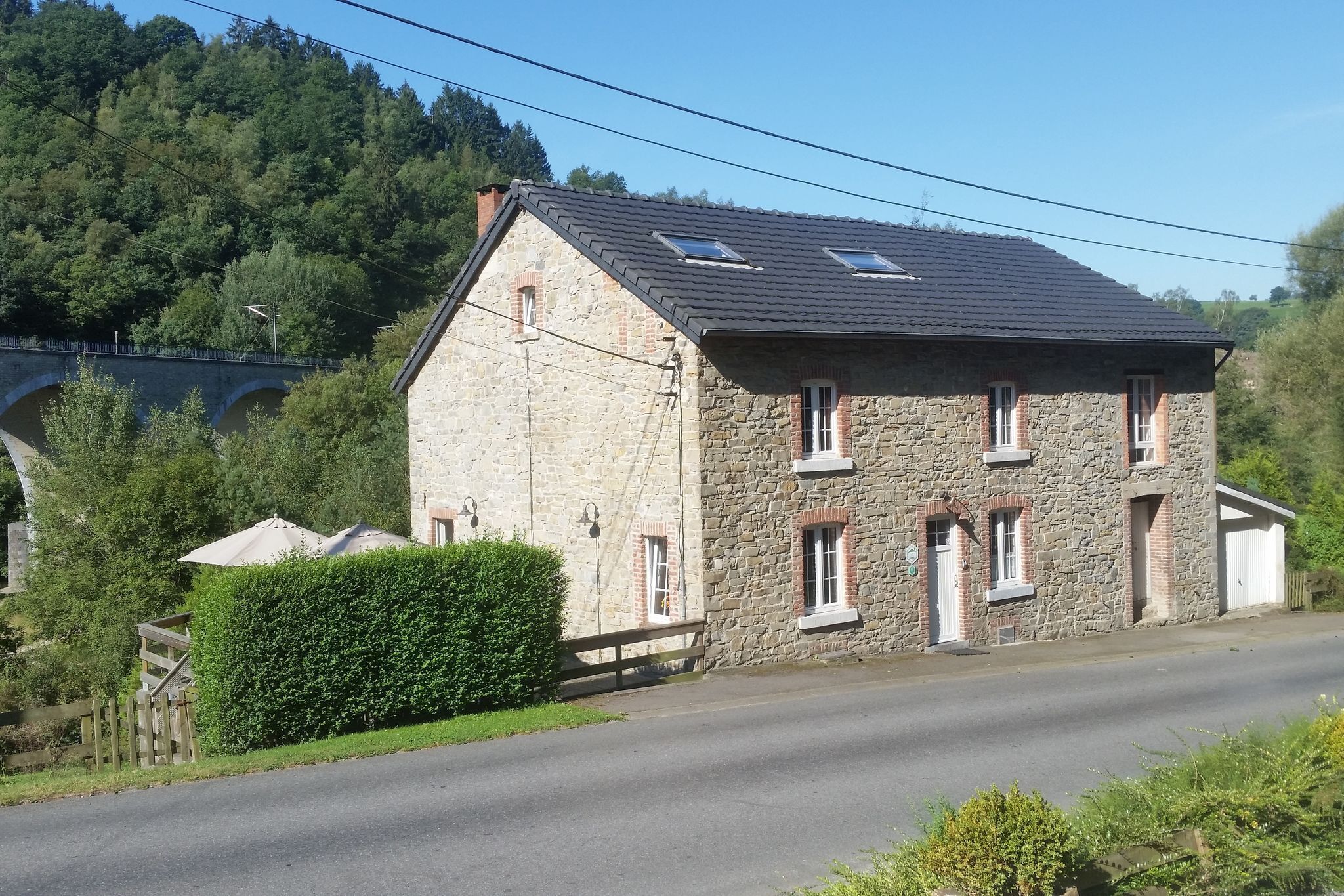 A stone building with a sloped roof, a small porch, and a paved road in front.