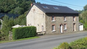 Ein Gebäude aus Stein mit einem geneigten Dach, einer kleinen Veranda und einer gepflasterten Straße davor.