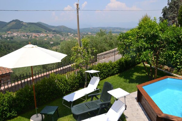 Ein Garten mit Swimmingpool, einem weißen Sonnenschirm und zwei Liegestühlen.
