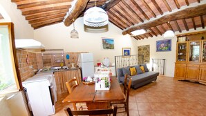 Una cocina acogedora con una mesa de comedor, sillas y un sofá. Hay un refrigerador, una lavadora y un armario con vajilla.