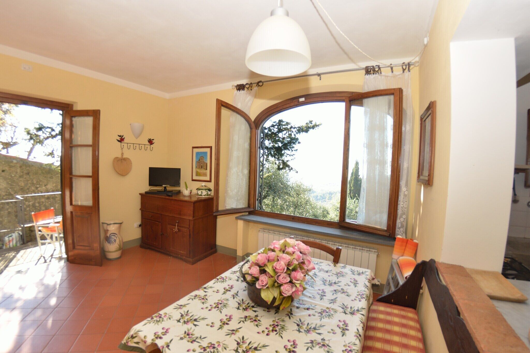 Un comedor con una mesa dispuesta para dos, un florero, un aparador de madera y una ventana con cortinas.