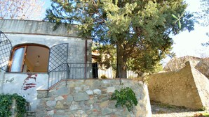 Un bâtiment rustique en pierre, avec une porte en bois, un portail en métal et un arbre en arrière-plan.