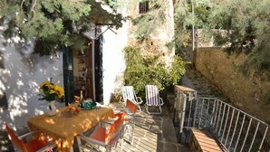 Une terrasse avec une table dressée pour deux personnes, entourée de chaises, d’un petit jardin et d’un mur en pierre.
