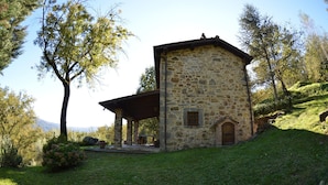 Un bâtiment en pierre doté d’un patio couvert, entouré de verdure et d’arbres.