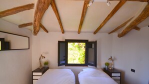 A bedroom with two beds, wooden beams, a window with a view of greenery, bedside tables with lamps, and a mirror on the wall. - Holiday House in Lucca with Pool & Valley Views (Borgo A Mozzano)