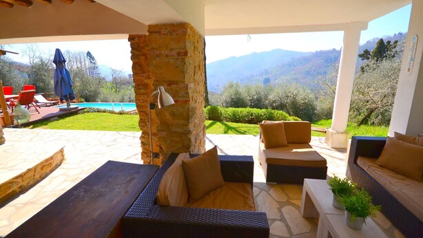 An outdoor patio area with stone flooring, wicker furniture, and a view of mountains. - Holiday House in Lucca with Pool & Valley Views (Borgo A Mozzano)