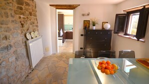 A kitchen with stone walls, a radiator, a glass table with a bowl of fruit, and a view into the dining area. - Holiday House in Lucca with Pool & Valley Views (Borgo A Mozzano)
