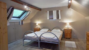 Ein Schlafzimmer mit Dachfenster, zwei Betten, Nachttischen mit Lampen, einem Holzschrank und einem kleinen Teppich auf dem Boden.