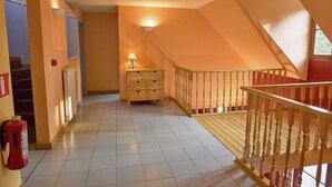 A hallway with a wooden staircase, a radiator, a fire extinguisher, and a lamp.