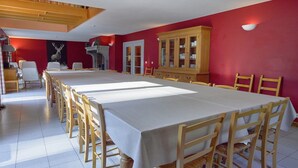 A dining area with a long table, wooden chairs, and a red wall.