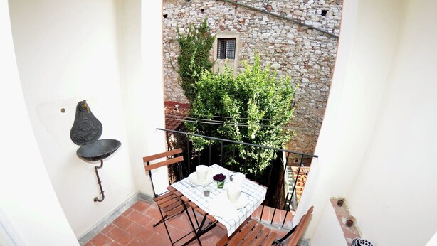 En lille balkon med et bord til to, en hængestol og en stenvæg med et vindue.