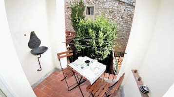 A small balcony with a table set for two, a hanging chair, and a stone wall with a window.