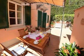 A wooden table set for tea with a view of a garden and a building with green shutters. - House in Ciciana with Pool and Scenic Views (Lucca)