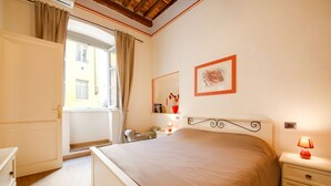 Ein Schlafzimmer mit Bett, Nachttisch, Lampe und einem Fenster mit Vorhängen.