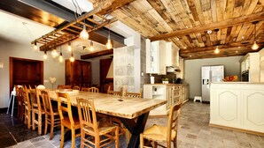 A spacious dining area with a large wooden table and chairs, a kitchen with white cabinets, and exposed wooden beams on the ceiling. - Magnificent Holiday Home in Baronville with Heated Pool & Billiards (Beauraing Ardennes)