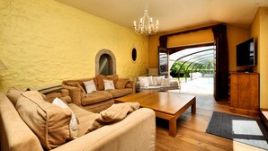 A living room with a large sofa set, a wooden coffee table, a chandelier, and a television. - Magnificent Holiday Home in Baronville with Heated Pool & Billiards (Beauraing Ardennes)