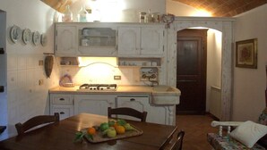 A kitchen with white cabinets, a stove, and a dining table with fruits. - Pisa Stay close to Leaning Tower (Pisa)