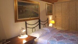 A bedroom with a bed, a nightstand with a lamp, a wooden wardrobe, and two framed paintings on the wall. - Pisa Stay close to Leaning Tower (Pisa)