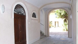 A hallway with a wooden door, stone steps, and arched doorways leading to an outdoor area with greenery. - Pisa Stay close to Leaning Tower (Pisa)