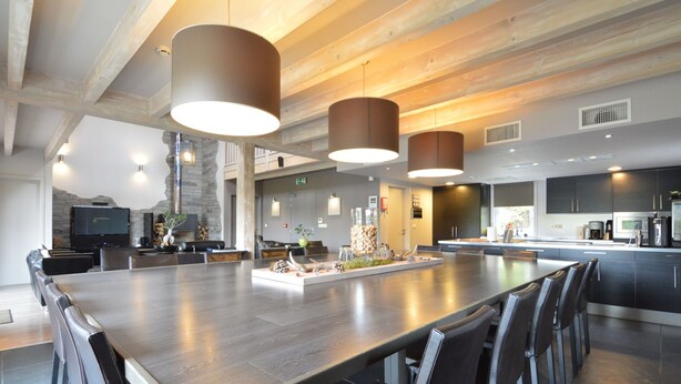 Un comedor amplio con una mesa larga, iluminación moderna y una cocina al fondo.